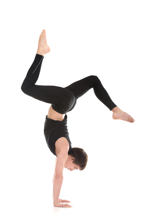 Sporty young man working out, dance, yoga, pilates, fitness training, doing Bent Legged Stag handstand, side view, full lengthの写真素材