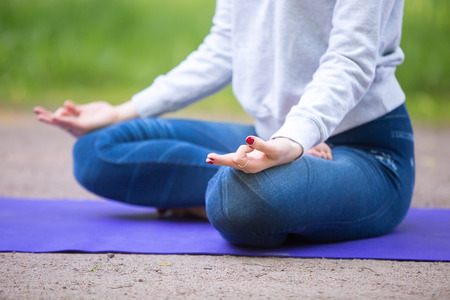 Close up of fingers of beautiful sporty young woman sitting cross legged in Ardha Padmasana, half lotus posture on blue mat on the street in park alley, meditating or breathingの写真素材
