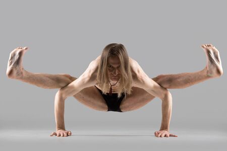 Sporty young yogi man standing in arm balance, variation of Firefly posture, asana Tittibhasana, studio shot on dark background, full lengthの写真素材