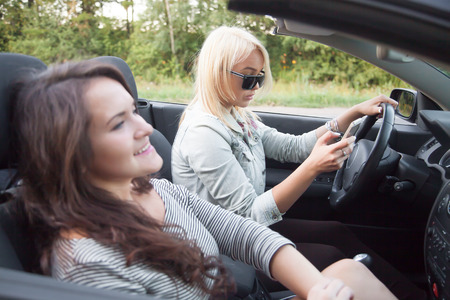Two beautiful traveler young women friends riding black sports car together, focus on serious busy...