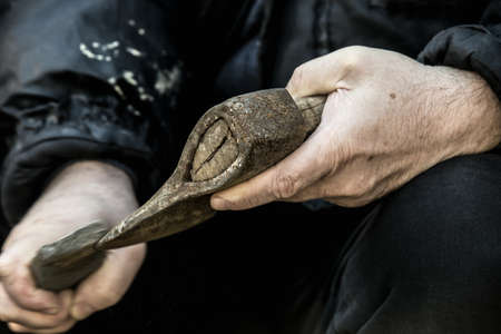 Close-up of male hands sharpening old rusty axe with a grindstone
