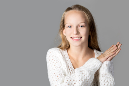 Portrait of happy beautiful casual caucasian teenage girl wearing white knitted sweater, clapping with excitement, studio image, gray background, copy spaceの写真素材