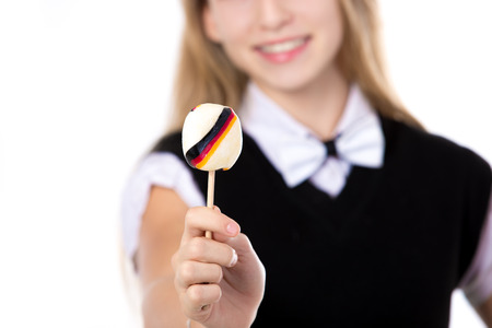 Happy cute beautiful blond girl wearing black formal outfit with bowtie, showing lollipop with Germany flag, studio shot, white background, close-up, focus on candyの写真素材