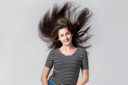 Portrait of beautiful young happy fit modern woman with flying hair, studio image on gray background