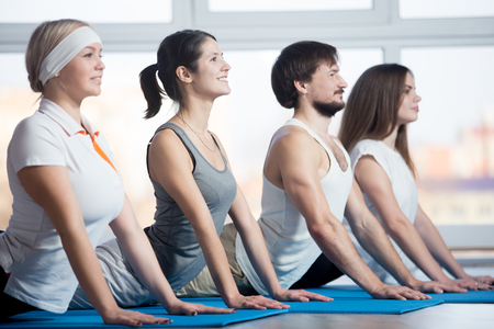 Fitness, stretching practice, group of four attractive smiling fit young people working out in sports club, doing Cobra posture, backbend exercise on blue mats in classの写真素材