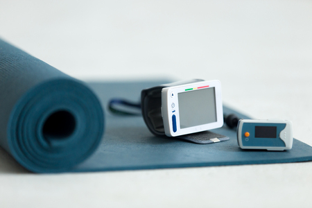 Rolled up blue yoga, pilates or exercise mat on the floor with modern medical equipment for checking blood pressure, pulse rate and oxygen, close upの写真素材