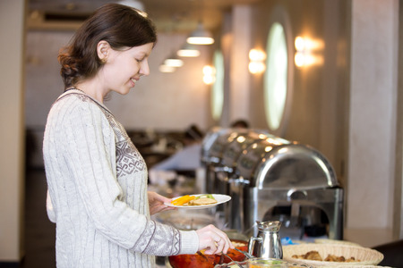 Portrait of young happy smiling woman getting self-catering breakfast in hotel restaurantの写真素材
