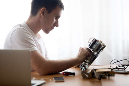 Portrait of handsome young computer repairman working with broken pc parts indoors in the home officeの写真素材