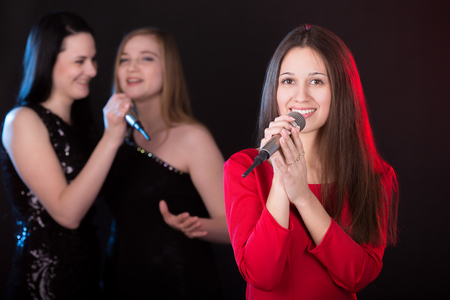 Portrait of beautiful smiling with bliss female singer with microphone, her friends singing on the backgroundの写真素材
