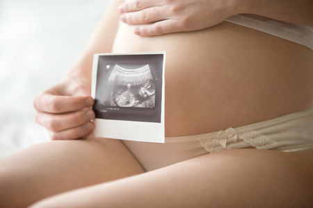 Close-up of belly of young pregnant model showing ultrasonic image of her baby. Future mom on her...