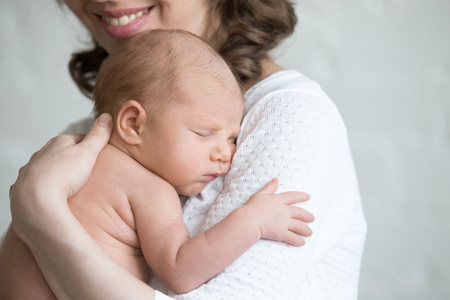 Newborn babe napping on woman arms. Young happy mother tenderly hugging sleeping adorable healthy new born child. Focus on little kid. Love, bonding, happy family concept. Close-up portraitの写真素材