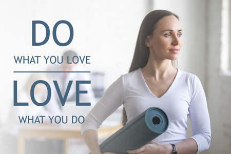 Business and healthy lifestyle concept. Portrait of beautiful sporty young office woman standing with yoga mat at workplace on break time. Motivational text "Do what you love, love what you do"の写真素材