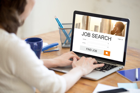 Young business woman working in office interior, searching for job online. Attractive female looking for job using web service on laptop. Back view over the shoulder. HR, recruitment, career conceptの写真素材