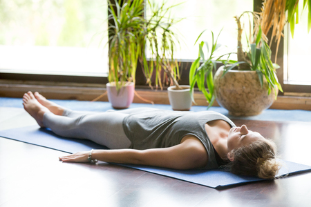 Attractive young woman working out at home, doing yoga exercise on blue mat, lying in Shavasana Corpse or Dead Body Posture , resting after practice, meditating, breathing. Full lengthの写真素材