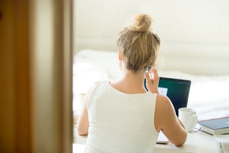 Woman sitting back talking on the phone at table with a cup and laptop on it. Rear view. Concept...