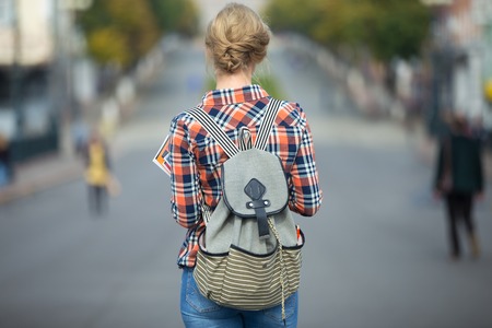 Young student girl walking down the street with a backpack, in the middle of the roadway. Back to school concept photo, back view, horizontalの写真素材