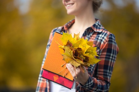 Smiling female young student outdoors holding yellow maple leaves, yellow background. Fall time. Back to school concept photo, closeup, horizontalの写真素材