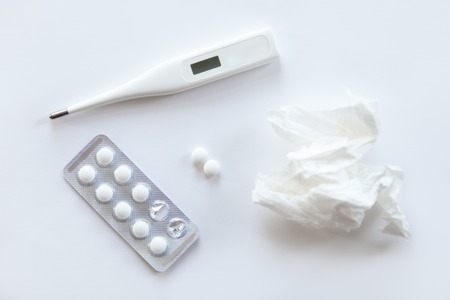 White desk with two round pills, taken from a foil case, thermometer, paper crumpled napkin on it. Top view, medicine concept photoの写真素材