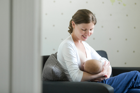 Portrait of a young attractive woman breastfeeding a child, holding on her knees. New born, bonding concept photo, view over the doorway, lifestyleの写真素材