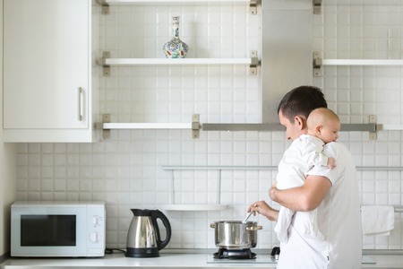 Man in the kitchen holding a child on his shoulder, cooking in the pan. New born, bonding concept photo, familyの写真素材