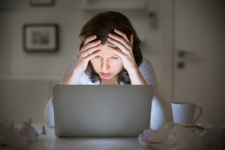 Portrait of a woman grabbing her head in despair at the desk near the laptop, late at night. Education, business concept photo. Lifestyleの写真素材