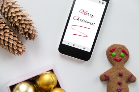 Flat view of a phone among cute Christmas decoration, cones, box of glass balls, ginger man....