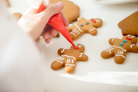 Close up of confectioner hand decorating a gingerman with a pastry bag, drawing a smile, making it...
