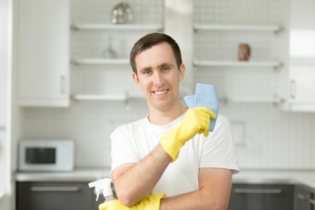 Portrait of smiling young man, wearing rubber protective yellow gloves, holding rag and spray bottle detergent. Home, housekeeping conceptの写真素材