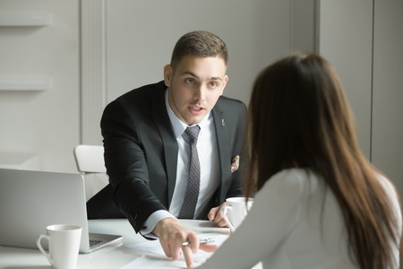 Young handsome businessman is pointing to a mistake in a paper, incorrectly done task by a woman or she is missing deadlines, showing his authority. Business concept photoの写真素材
