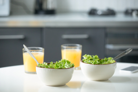 Two bowls of salad and glasses of orange juice on a white kitchen table. Healthy breakfast for couple. Light snack to promote a healthy day, vegetables as part of daily dietの写真素材