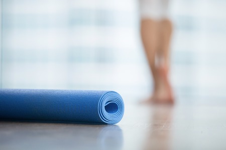 Close up of yoga, fitness, foam exercise mat fix in a roll in living room or fitness center, blurred female body at the background, resting after yoga, fitness class. Healthy lifestyle conceptの写真素材