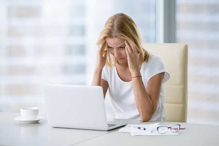 Young attractive woman at modern office desk, working on laptop, massaging temples to forget about constant headaches, noisy loud office giving a migraine, relieving stress, chronic pain, help soothe Young attractive woman at modern office desk, working on laptop, massaging temples to forget about constant headaches, noisy loud office giving a migraine, relieving stress, chronic pain, help soothe