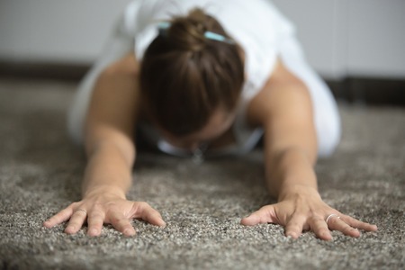 Sporty young woman practicing yoga, sitting in Child exercise, Balasana pose, working out, resting after training, wearing white sportswear, indoor, home interior background, closeupの写真素材