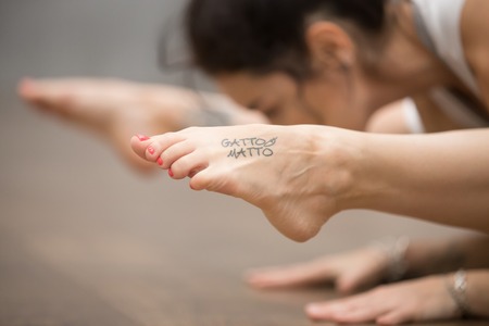 Attractive young woman with beautiful tattoo on her foot meaning Wild kitty working out on the floor, doing yoga, pilates balancing exercise. Close up of footの写真素材