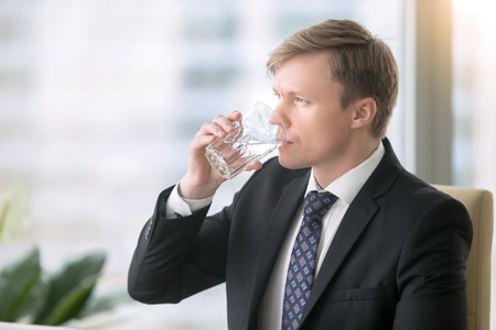 Young handsome businessman, drinking water, feeling tired foggy thinking and poor concentration, hot summer, feeling leaner and fitter, water supply in the officeの写真素材