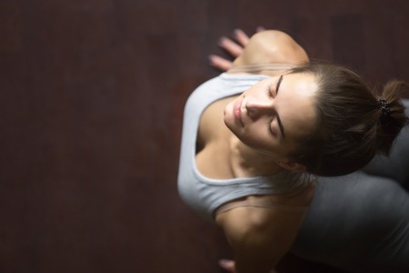 Beautiful young happy model girl working out in home interior, doing yoga exercise on wooden floor, stretching in upward facing dog or cobra pose. High angle view. Copy spaceの写真素材