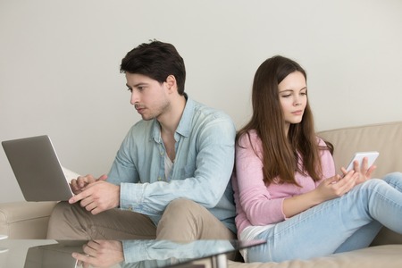 Young couple sitting back to back at home using laptop computer and tablet, internet addiction,...