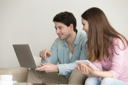 Young people with electronic devices indoors, man using laptop computer, woman holding tablet, downloading apps, social networking, online shopping, mobile banking, self-employed freelancersの写真素材