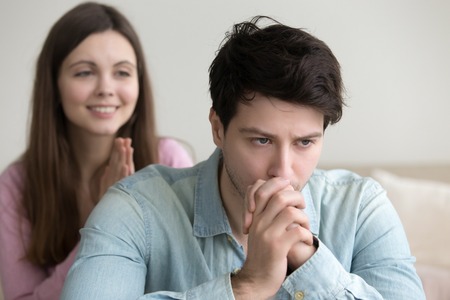 Sad frustrated guy thinking about accepting or rejecting apology of a girl. Offended boyfriend angry at woman made mistake, being late, cheating, wasting money. Excuses, saying I m sorry, pleaseの写真素材