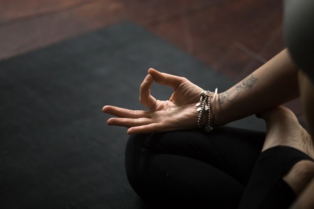 Close up of young woman hand with tattoo and wrist bracelets practicing yoga, sitting in Padmasana exercise on black mat, Lotus pose with mudra gesture, working out, meditating, copy space backgroundの写真素材