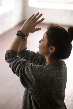 Young attractive yogi woman practicing yoga concept, making namaste gesture, working out, wearing...