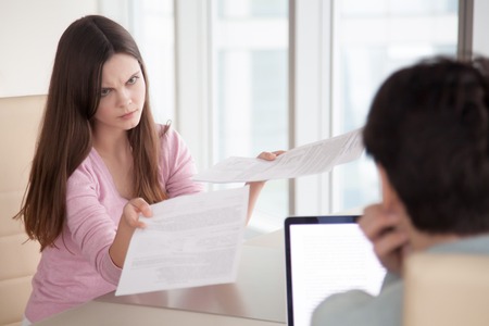 Angry businesswoman showing partner financial reports, documents, contracts, lady boss dissatisfied with work results, female manager mad at coworker due to paperwork error. Couple arguing over billsの写真素材