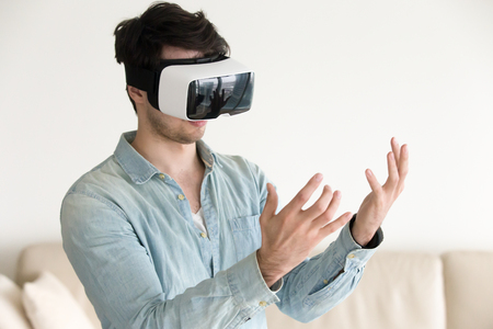 Trying VR headset for the first time at home, young guy looking at his hands wearing virtual reality...