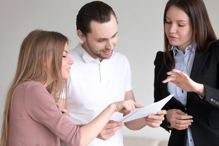 Male client holding documents and attentively studying them, discussing offer with female manager and wife, terms and condition of contract agreement, considering bank loan, health personal insuranceの写真素材