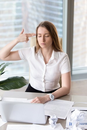 Overworked busy businesswoman wants kill herself because of difficult work and fatigue. Tired office worker showing finger gun aimed at the head. Exhausted female entrepreneur with suicidal thoughtsの写真素材