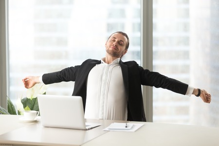 Businessman stretching out at desk with laptop. Office worker doing relaxing exercises at workplace to relieve physical fatigue Manager make deep breath of fresh air, relaxed after finishing workの写真素材