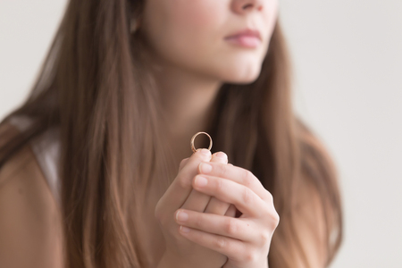 Close up photo of golden ring in womans hands. Lonely young lady worries about breakup with lover, thinking about future with wedding ring in hands. Engagement, proposal of marriage or divorce conceptの写真素材