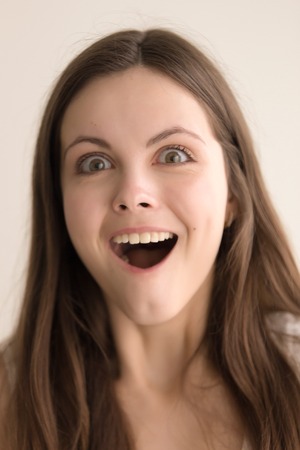 Headshot portrait of pleasantly surprised young woman. Adorable teenager girl with astonished facial expression looking at camera with joy. Beautiful lady feeling impressed. Close up. Front viewの写真素材