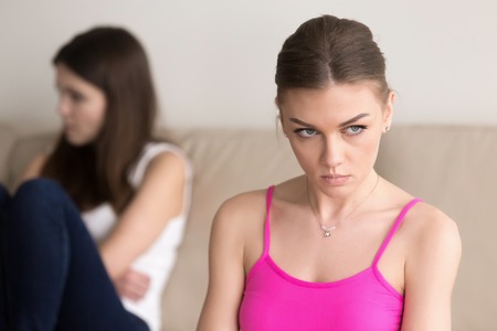 Headshot portrait of grumpy young woman sitting next to offended girlfriend after argument. Frustrated lady hating her friend, feeling wrath and dissatisfied because of conflict, ignores the opponentの素材 [FY31083281932]