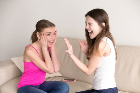 Happy woman yelling while showing her precious engagement ring on finger to her surprised girlfriend. Adorable ladies celebrating wedding proposal, exited because of romantic gift, getting jewelryの写真素材